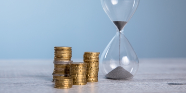 Hourglass with coins on the gray background.